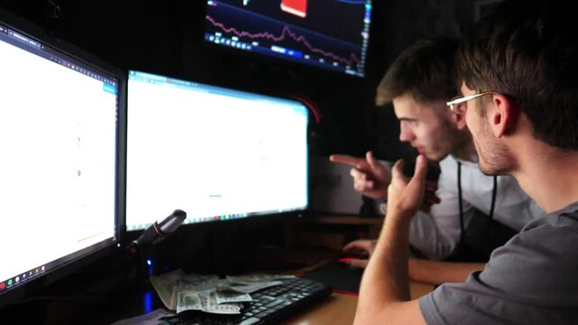 Two traders engaged in cryptocurrency analysis, focused on multiple screens displaying market data, with cash on desk, illustrating the dynamic environment of digital trading and investment strategies