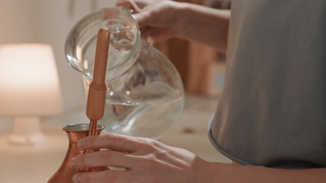 Closeup hands pouring water into copper pot glass kettle and coffee grounds in soft focus, lamp glow in background, precise slow pour, warm steam and tactile detail capturing quiet sensory ritual