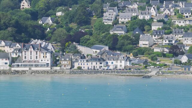 Aerial view of the coastal town of Binic in Brittany, France, showing a scenic beachfront lined with traditional houses, a ferris wheel, and people enjoying the sandy beach.