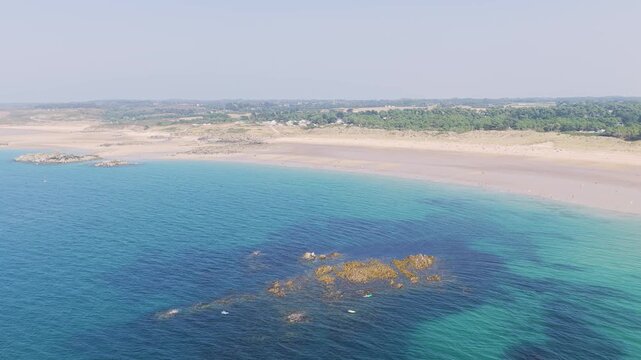 Aerial view of the sweeping coastline of Anse du Croc in Frehel, Brittany, France with the video showcases turquoise waters, sandy beaches, rocky outcrops.