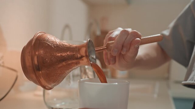 Closeup pouring Turkish coffee into mug, copper cezve and wooden stirrer on kitchen countertop with soft lamp glow intimate morning ritual, careful stirring and foam forming, home musician savoring