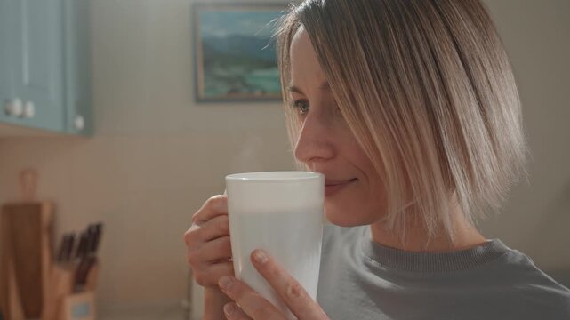 Woman in kitchen sipping coffee, music lover mood, gentle smile, white mug, warm sunlight, short bob haircut, relaxed morning routine, acoustic melody implied, cozy domestic atmosphere.