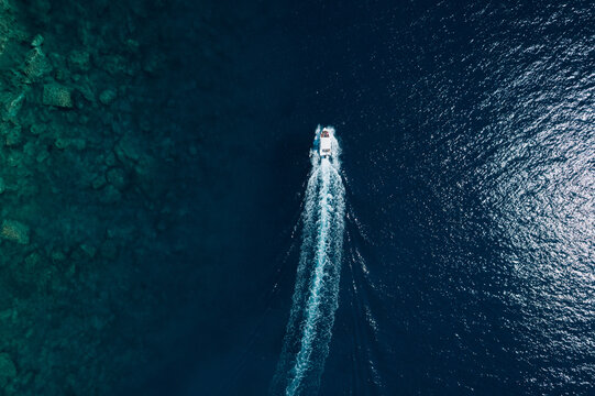 Scenic aerial seascape featuring a fast boat, crystal clear water, rocky seabed, sunlight reflections and a beautiful marine landscape.