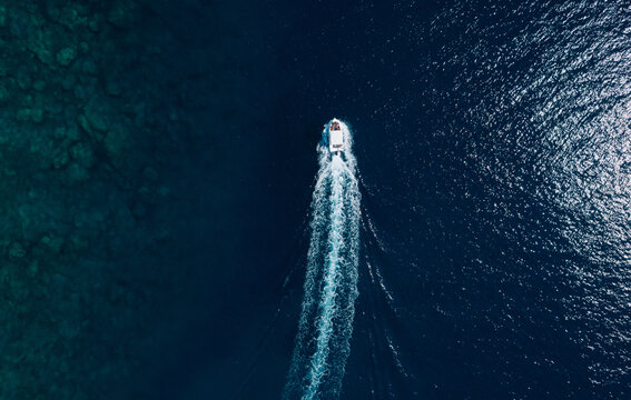 High angle view of a motorboat speeding through deep blue ocean water with a long white wake and visible underwater reef.