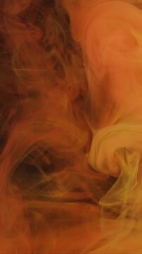 Vertical video. Smoke background. Cloud ink. Blur orange yellow colorful fume liquid exhaust chemical texture fluttering on dark black abstraction.