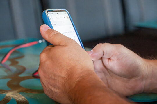 a person's hands holding and actively using a smartphone with a blue protective case, resting above a patterned teal table.