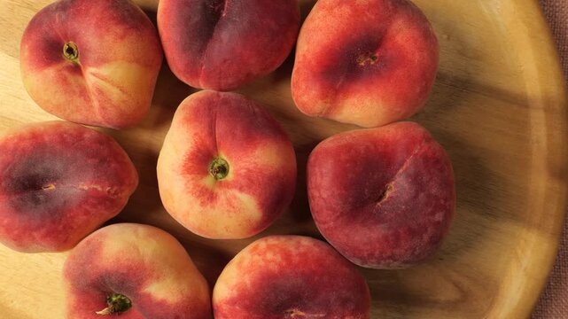 Fresh ripe flat peaches slowly moving on a wooden plate
