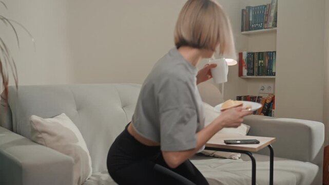 Cozy living room morning coffee scene showing music lover enjoying quiet breakfast on sofa. Young songwriter flips through sheet music, student skims book, baker samples pastry, remote worker checks
