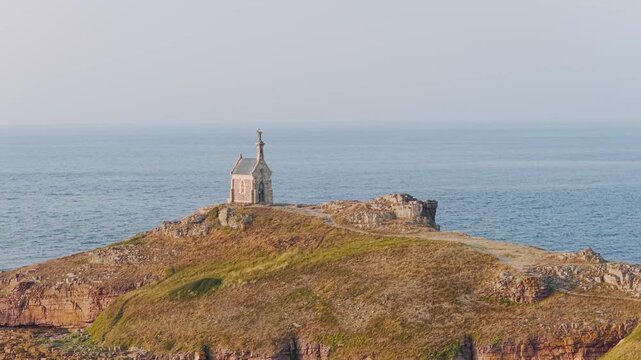 A solitary stone chapel stands atop the rugged cliffs of Ilot Saint Michel, overlooking the vast blue sea near Erquy in Brittany, France.