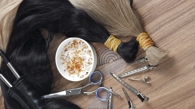 Natural human hair extensions prepared for hot fusion keratin bonding. Keratin tips, hair extension tools and clips arranged on a salon workstation, illustrating professional hair extension applicatio