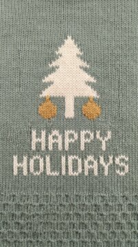 knitted holiday greeting with tree and ornament design on green fabric background