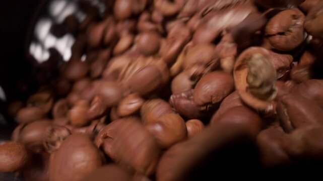 Slow motion coffee beans tumbling inside roaster drum in industrial roastery interior, food industry macro probe view.