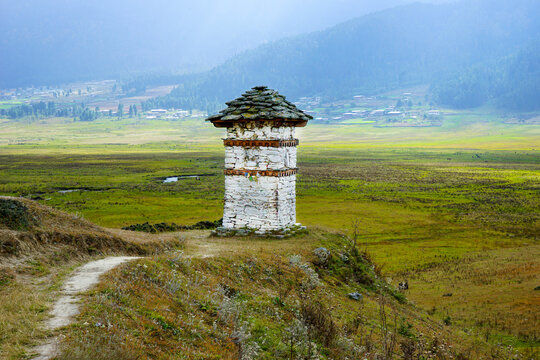 Bhutan, beautyful valley  in central Bhutan. A Small praying tower beside a trail with  foggy mountains in the background.
