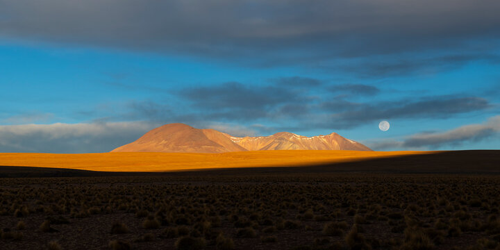 Full moon and Andes mountains at sunset panorama, Siloli Desert, Uyuni, Bolivia.