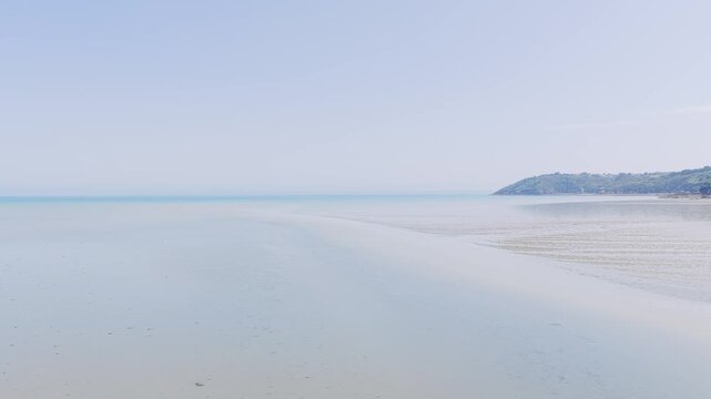 A tranquil, wide-angle shot of Binic beach on the Brittany coast in France, captured during low tide on a clear summer day.