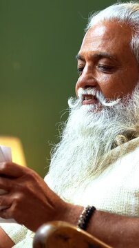 Indian mid age bearded man holds photographs prints while sitting on rocking chair at home, stylish male with wet eyes recalling precious memories of loved one in modern interior lifestyle