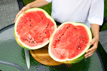 Young boy holding apart two freshly cut halves of a ripe watermelon outdoors. Fresh seasonal fruit and healthy summer eating concept. © Olena Smerichka