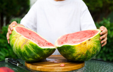 Young boy holding apart two freshly cut halves of a ripe watermelon outdoors. Fresh seasonal fruit and healthy summer eating concept. © Olena Smerichka