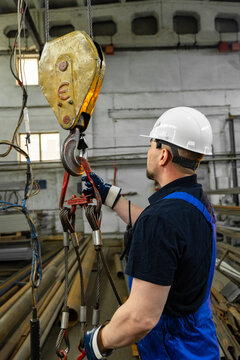 Industrial worker inspecting crane hook and wire rope slings in factory