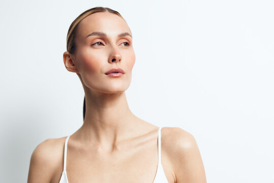 Close up portrait of a calm woman with clear skin on a white background, emphasizing natural beauty, skincare, and self care through soft studio lighting