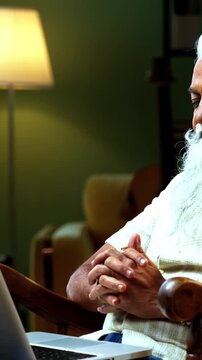 Indian mid age bearded man watching funny movie on laptop sitting on relaxing chair at home, stylish mature male enjoying online streaming entertainment with laughter in modern interior