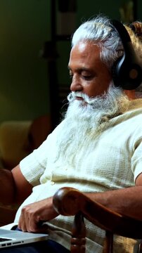 Indian mid age bearded man watching funny movie on laptop sitting on relaxing chair at home, stylish mature male enjoying online streaming entertainment with laughter in modern interior