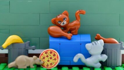 Fototapeta premium Tambov, Russian Federation - August 03, 2026 A close-up shot of Lego cats and rat minifigure searching for food like pizza and chicken near trash cans.