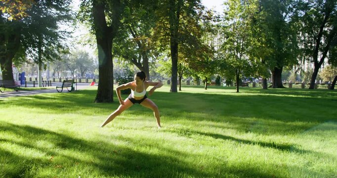 Yoga park. Outdoor fitness. Flexible active woman practicing sportive workout doing physical exercise in sunlit green atmosphere.
