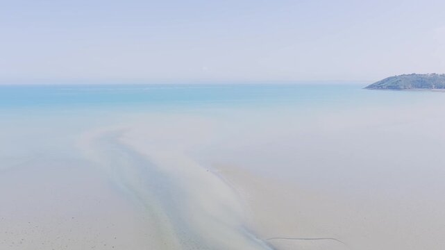 Aerial view of the expansive sandy beach of Binic during low tide, with gentle waves meeting the shoreline and a distant headland under a clear blue sky.