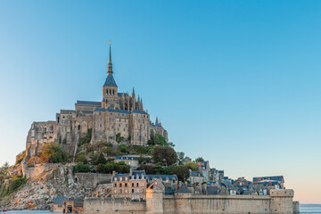 Obraz premium Close up view of Mont Saint-Michel Abbey and fortified village at sunset in Normandy, France. Tidal island with monastery in Normandie. French architecture. Cultural tourism and European landmarks