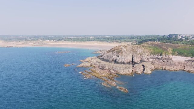 Aerial view of Anse du Croc in Frehel, Brittany, France, showing a rugged rocky coastline, clear blue sea, and sandy beaches under a bright summer sky.