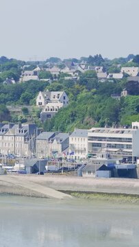 A scenic view of Binic, a coastal town in Brittany, France, showing the beach, marina, and residential buildings nestled among green hills.