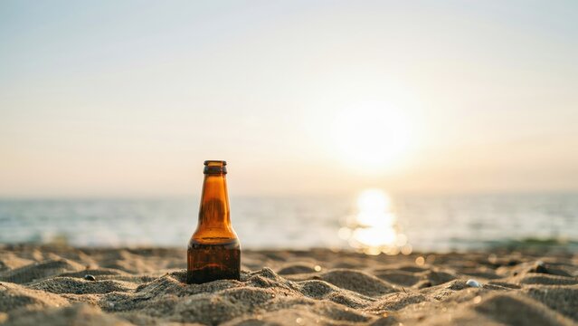 Amber beer bottle standing in sand on a beach at sunset
