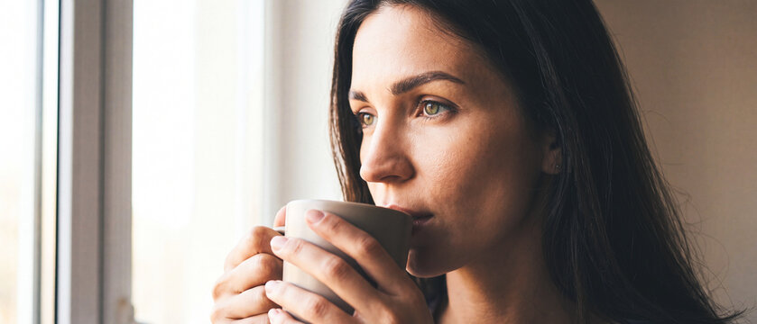 Woman sips warm drink by window morning light