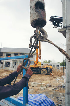 Man hand pulling metal sling of crane to lift cement platform at construction site-vertical image.