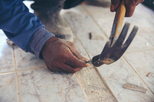 Worker hand Hammer hits nail at construction site. Man hold tool for repair of tile and concrete floor, builder works on home renovation project inside building background space
