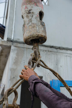 Man hand pulling metal sling of crane to lift cement platform at construction site-vertical image.