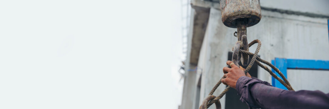 Man hand pulling metal sling of crane to lift cement platform at construction site-banner image.