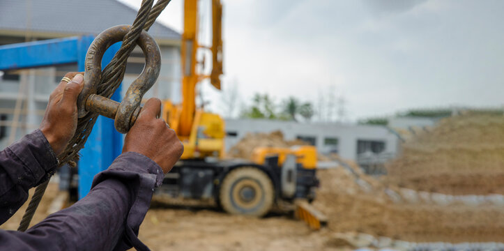 Man hand pulling metal sling of crane to lift cement platform at construction site-banner image.