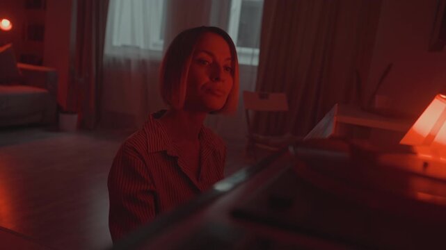 Woman enjoying music. Reading record cover with warmth. Contemplative lady immersed in nostalgic music moment. Soothing red glow illuminates woman as she explores vintage record sleeve carefully
