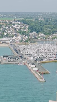 A high-angle aerial shot showcasing the marina of Binic, with numerous sailboats and yachts docked in the harbor, surrounded by the picturesque coastal town.
