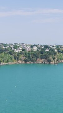 A wide view of the turquoise sea with a rocky coastline and the town of Binic in the background.