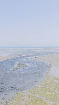 Wide static shot of Binic beach in Brittany, France, during low tide with the sandy shore is exposed with shallow water channels and patches of green seaweed.