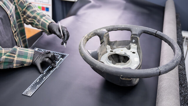 A seamstress in a workshop makes a new leather cover for a car steering wheel.