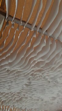Decorative white fabric drapery gently moving and rippling in the air, creating a dynamic suspended textile ceiling with a soft flowing texture. Abstract architectural background with neutral tones an