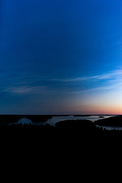 Zoom in aerial view of island under rare noctilucent clouds in dark blue night sky in Finland