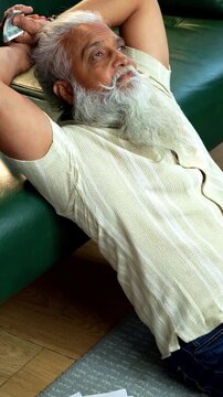 Indian mid age bearded man counting cash Indian rupees and relaxing between work sitting on carpet in modern home, stylish mature male managing household finance and budget indoors