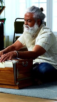 Indian mid age stylish bearded man practicing vocals or singing at home, dedicated to daily riyaz while accompanying harmonium in modern home studio interior setting
