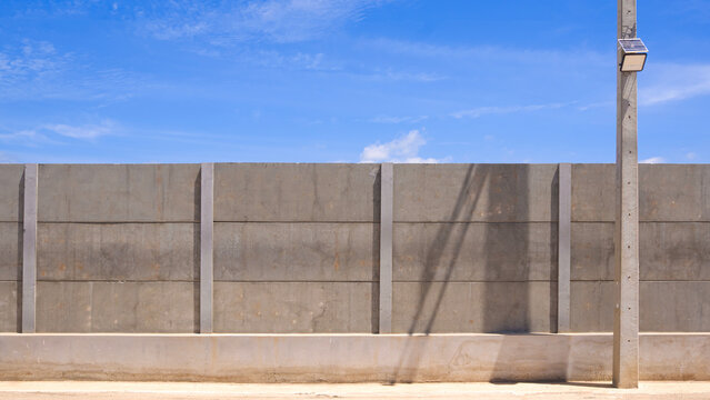 Precast concrete wall fence with solar street light hanging on electric pole under bright blue sky.