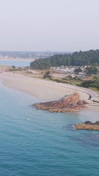 Aerial view of Plage Saint Michel in Erquy, Brittany, France, showing a sandy beach, turquoise sea, rocky outcrops, and a forested area with holiday accommodations in the background.